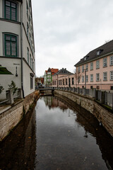 A calm canal flows between historic façades, captured in a vertical composition under soft grey daylight and reflecting the surrounding architecture.