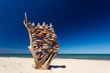 stack of multicolored balanced stones on an old wooden snags, on a blue sky and sea background