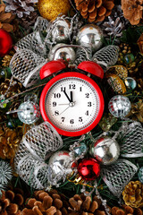 The bright red alarm clock shows five minutes to midnight. A New Year's composition with cones and Christmas toys.