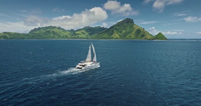 Fiji: travel destination, luxury catamaran sailing deep blue sea near tropical island, offering breathtaking views and sense of freedom and adventure. Remote wild nature paradise. Drone flight footage