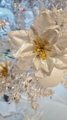 A shimmering silver poinsettia ornament with golden details decorates a bright white Christmas tree. Symbolizes festive elegance, winter beauty and the sparkle of holiday celebration