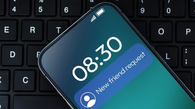New friend request notification received on the smartphone screen 4k footage close up with keyboard in the backdrop 