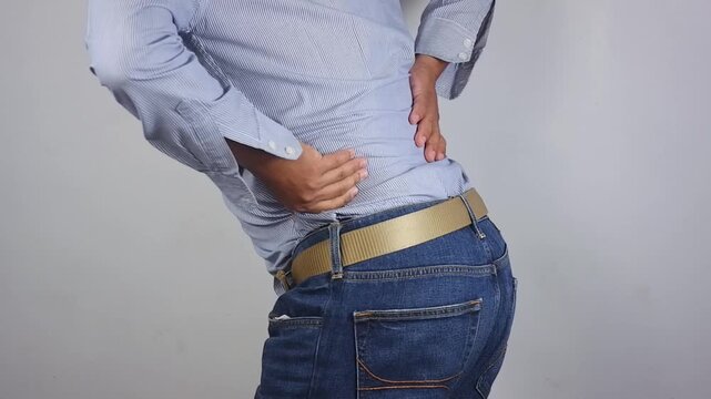 Lower back pain, young man experiencing lower back pain after working from home. An adult man holding and massaging his lower back, chronic back pain, bone calcification, osteoporosis. Healthcare conc