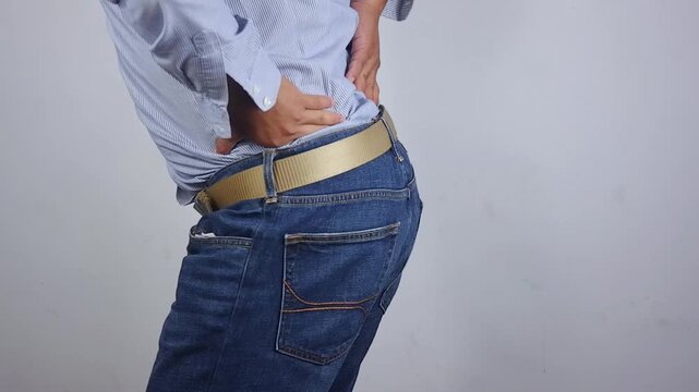 Lower back pain, young man experiencing lower back pain after working from home. An adult man holding and massaging his lower back, chronic back pain, bone calcification, osteoporosis. Healthcare conc