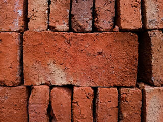 A close-up view of a large, tightly stacked pile of rough red bricks, showcasing the gritty texture and uniform pattern of basic construction materials for a building project.