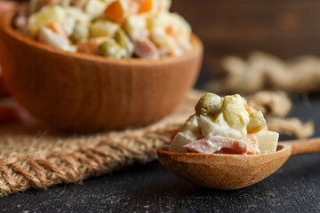 Close-up of a spoonful of Olivier salad with a wooden bowl in the background