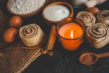 Cozy cinnamon rolls with ingredients and a warm candle on a dark background