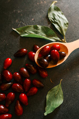 Fresh dogwood berries in a wooden spoon with green leaves on a dark surface