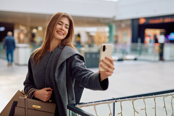 Happy young woman holding smartphone taking selfie while shopping. Lifestyle concept enjoying...