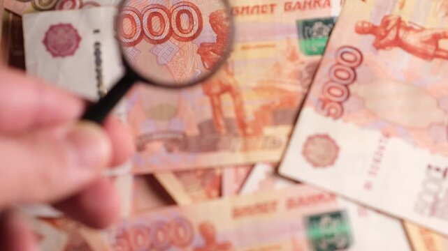 Close examination of different currency notes using a magnifying glass reveals intricate details and security features for verification.