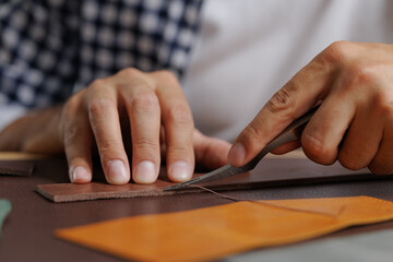 Hand of male crafting leather with precision knife and tools