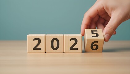 A hand placing a block to change the year from 2025 to 2026 on wooden cubes.