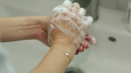 A person washes their hands thoroughly with soap at a bathroom sink, demonstrating a proper hand cleaning technique for hygiene.