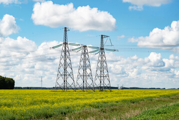 power line tower against blue sky and clouds over yellow field in summer