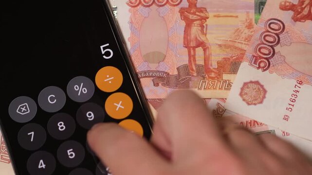 A person uses a calculator to add up cash notes while sitting in a comfortable area at home.