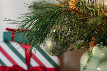 Close-up of a fir branch decorated with Christmas ornaments and wrapped gifts on the background.