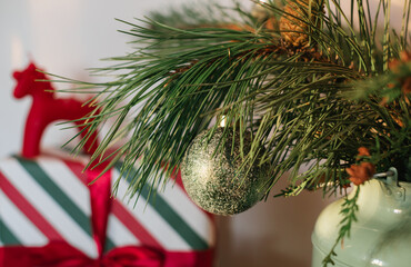 Close-up of a fir branch decorated with Christmas ornaments and a red horse on top of wrapped gifts on the background.
