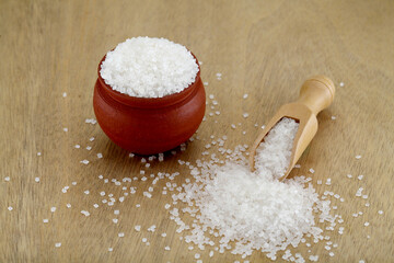 White sugar spilled out of clay pot and wooden scoop