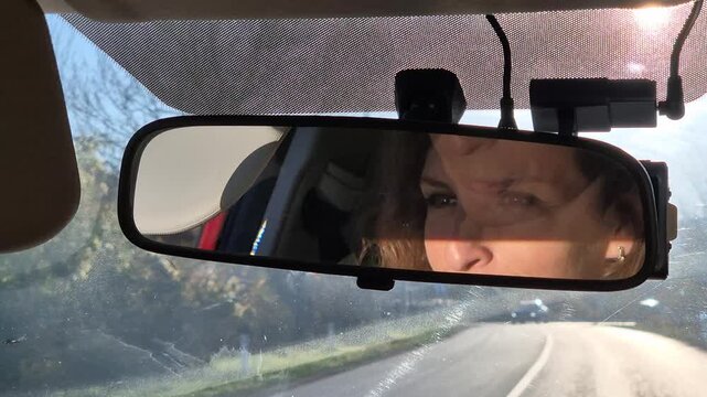 Driving woman road trip. Female reflection visible in car rearview mirror while traveling the highway on a sunny day.
