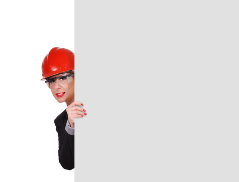 A businesswoman engineer in glasses and a red helmet looks out from behind a white blank wall.