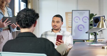 Diverse coworkers entering meeting room to discuss progress, man scrolling phone pointing to charts