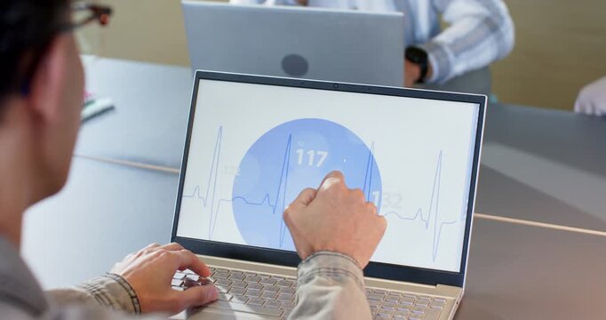 Man tapping touchscreen laptop at meeting table is animating ECG overlay and displaying heart rate