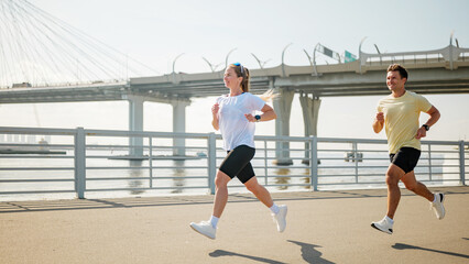Fototapeta premium Couple running along riverside path in sunny weather