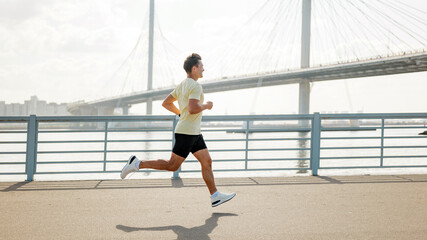 Man jogging near a bridge by the water during daytime