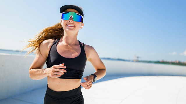Woman running in activewear with sunglasses on a track