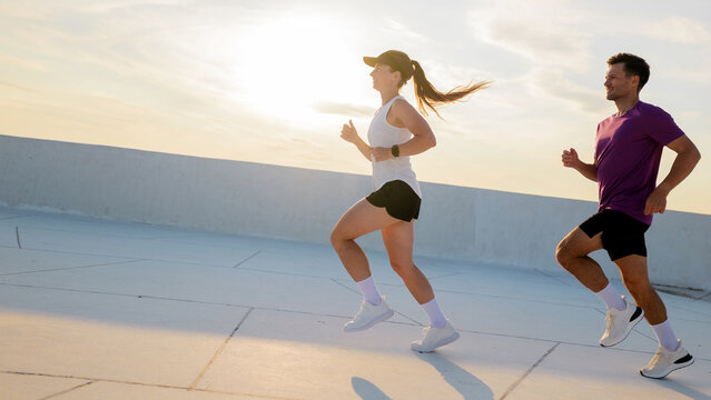 Young couple jogging on rooftop terrace during sunset