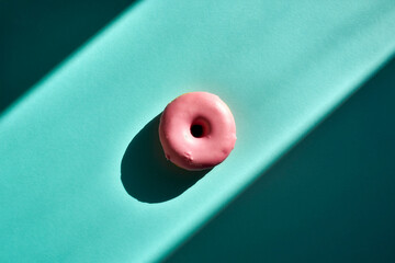 Single pink glazed donut on vibrant teal background with harsh diagonal geometric shadows, top view