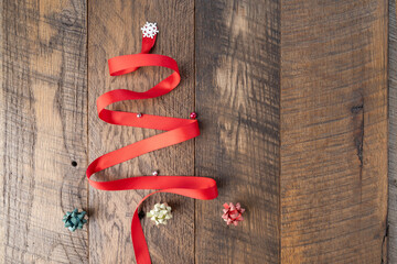 Red ribbon Christmas tree shape on a wooden background with bows, ornaments, and snowflake.