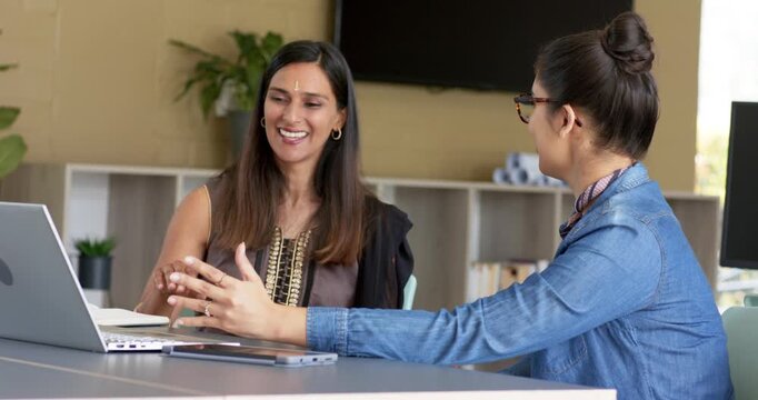 Diverse female colleagues at office pointing at laptop talking offering tablet reviewing content