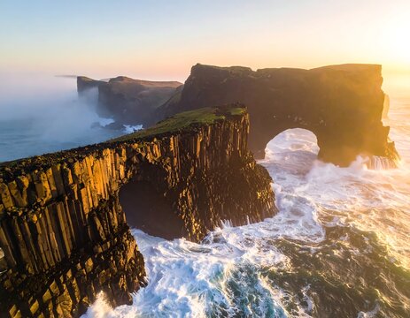 Aerial view of a rugged coastline at sunset, with wave-cut arches