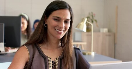Indian woman reading notification on silver laptop at office desk, smiling before resuming typing - Powered by Adobe