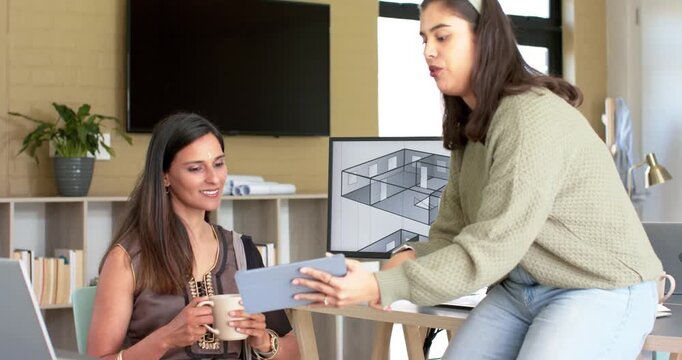Diverse female coworkers tapping tablet, displaying 3D floorplan and discussing layout in office