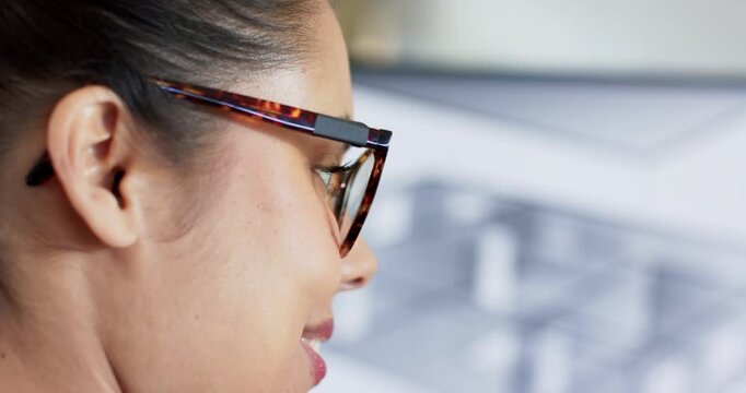 woman wearing glasses sitting at desk gazing at blurred monitor and smiling, revealing dimple
