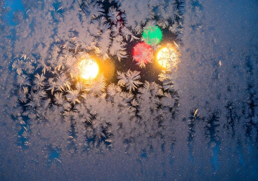 Frost pattern on window glass with colorful bokeh lights in background