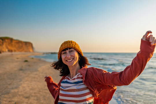 Happy cheerful girl having fun on the beach. Attractive stylish woman running on the beach waving her arms. Smiling cheerful lady having fun on the seashore.