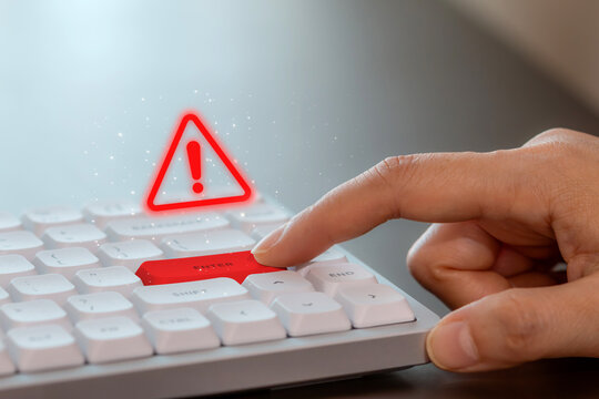 A finger presses a red "Enter" key on a white keyboard, with a warning sign, symbolizing caution in cyber security and data risk