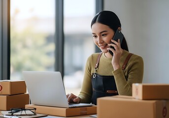 A Focused Young Asian Woman Manages Her Online Business, Talking On The Phone While Using A Laptop. Numerous Shipping Boxes Surround Her In A Home Office Setting.