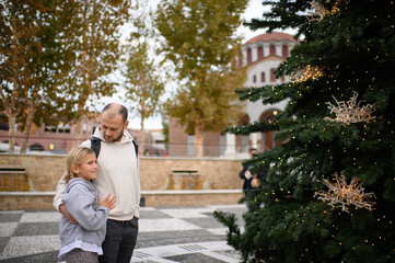 Fototapeta premium Father and daughter walking through the city, admiring Christmas decorations and festive lights, enjoying a joyful winter outing together in a holiday atmosphere. 