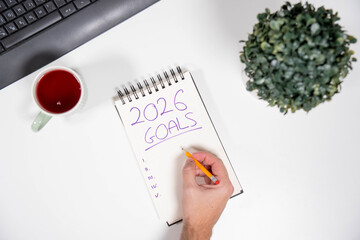 POV of a male hand writing a 2026 Goals list on a notepad. Represents taking action, commitment, business planning, and setting targets.