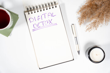  Digital Detox text on a notepad surrounded by calming elements like a candle and tea. Concept of mental health, unplugging from technology, and wellness.