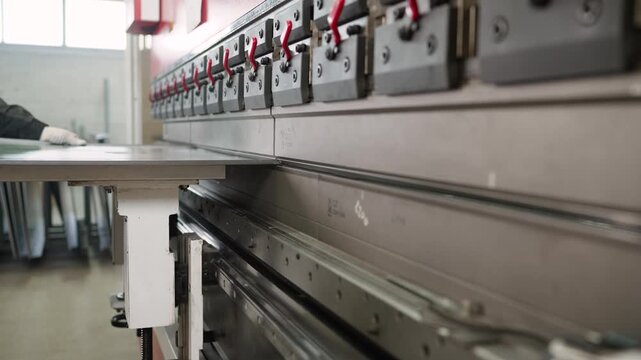Close-up of an automated hydraulic press brake bending a metal sheet. An industrial worker is operating the machinery in a factory