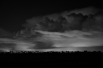 Powerful nighttime thunderstorm captured in black and white, with lightning striking above a...