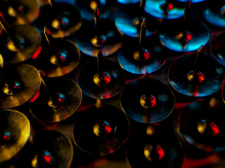 Cluster of metallic thumb tacks arranged closely together, illuminated with vivid red, blue, and gold lighting. 