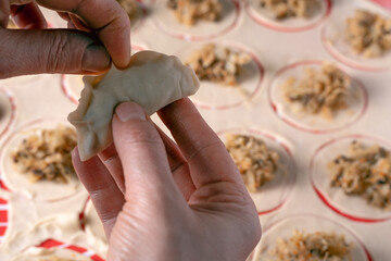 A pair of hands is shown folding the circular dough over the sauerkraut and mushroom filling to begin the sealing process of a polish dumpling