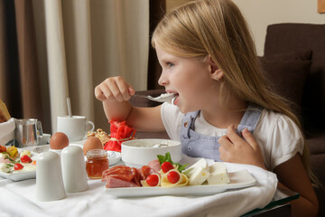 Cute little girl having breakfast, cereals with yogurt, tasty and healthy choice between various...