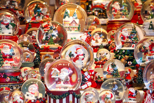 Colorful Christmas snow globes with Santa figures and winter village scenes on display at a festive market, showcasing holiday decorations, bright lights, and cheerful handcrafted details. - Powered by Adobe